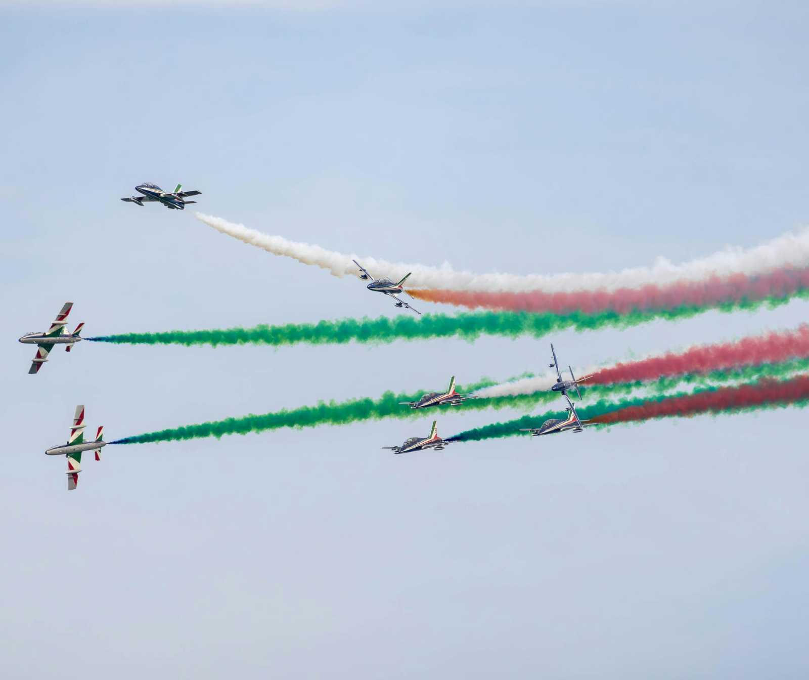 mehrere Kunstflugzeuge fliegen in Formation durch einen klaren Himmel und hinterlassen Rauchstreifen in den Farben Grün, Weiß und Rot.