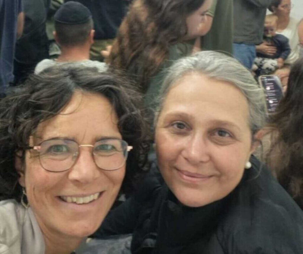 Selfie zweier Frauen. Sie lächeln; im Hintergrund sind weitere Menschen zu sehen, einer trägt eine Kippa