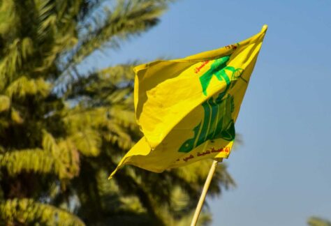 die Fahne der Hisbollah weht vor Palmen. der Himmel ist blau