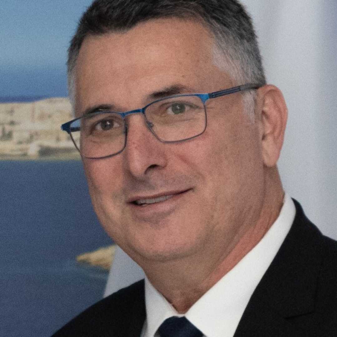 Ein Portraitfoto eines Mannes mittleren alterns mit Brille und Anzug. Er lächelt freundlich